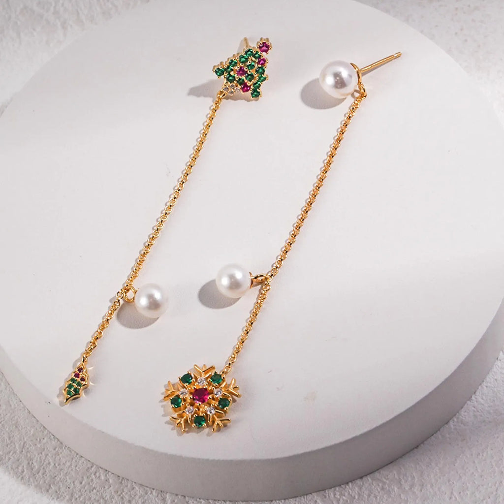 A pair of asymmetrical gold dangle earrings displayed on a white surface. One earring features a sunburst pendant with multicolored gemstones and a chain leading to a large pearl, while the other has a similar chain attached to a small gold butterfly and ends with a pearl. The unique design combines playfulness with elegance.