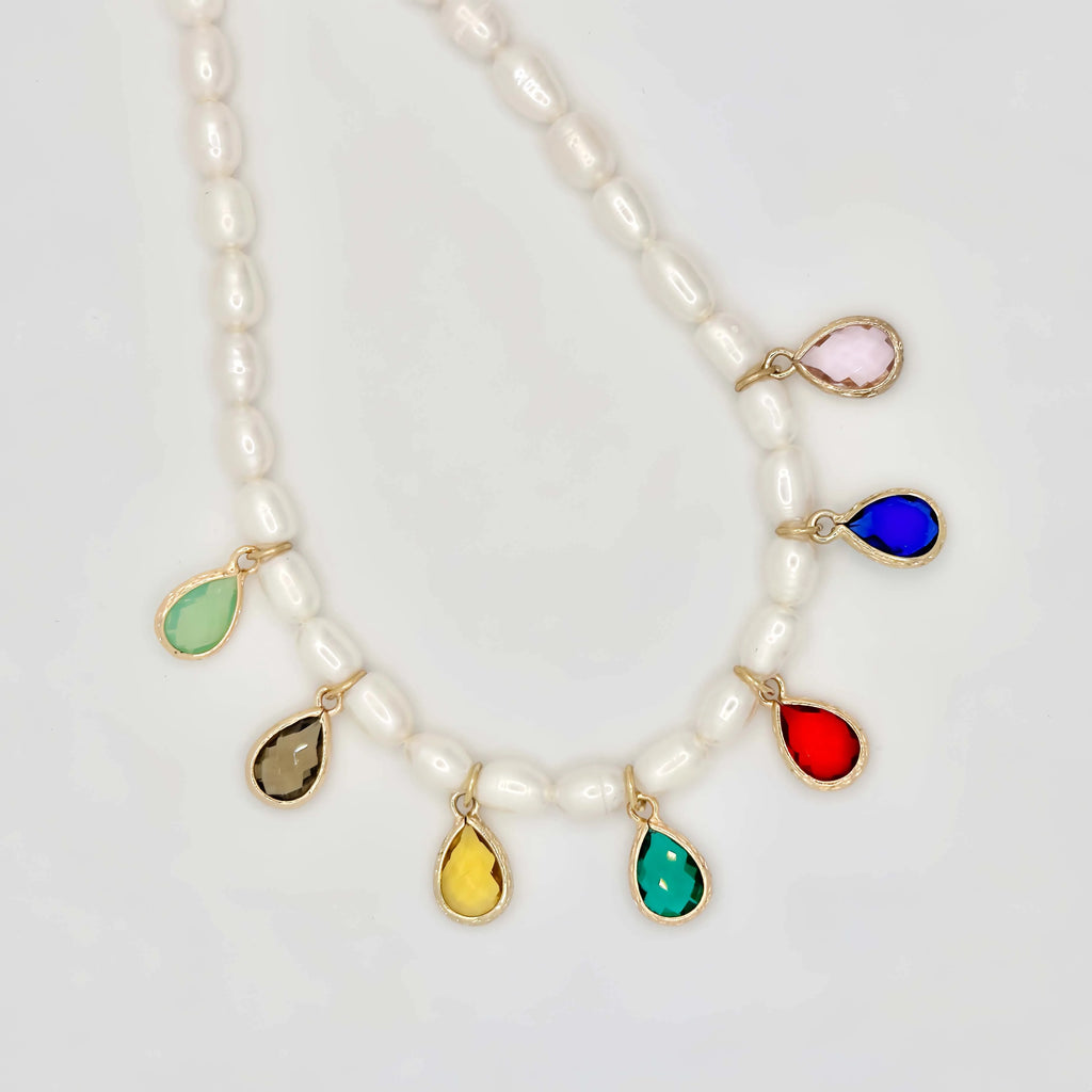 A luxurious pearl necklace and bracelet set displayed on a white background. The necklace is a string of round white pearls, interspersed with gold links and teardrop-shaped colored gemstones in bezel settings. The bracelet mirrors the design with similar colored gems and smaller pearls, both creating a harmonious and opulent look.