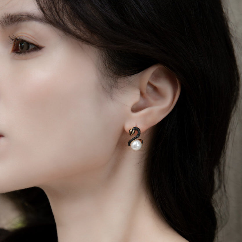 A close-up view of a woman's profile showcasing a unique earring. The earring features a black serpentine design with delicate crystal embellishments, leading down to a classic white pearl. The design gives a contemporary twist to the timeless pearl earring, blending modernity with elegance.