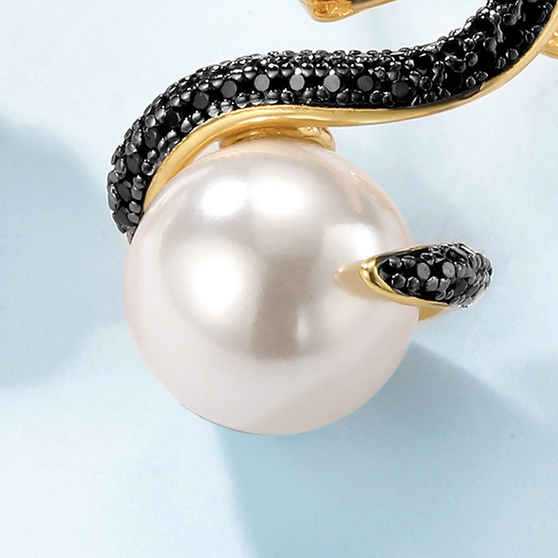 A close-up of an exquisite gold ring with a serpentine motif, coiling around a large, lustrous white pearl. The snake's body is encrusted with black crystals, and its head, highlighted in gold, contrasts strikingly with the pearl, creating a luxurious and captivating piece of jewelry.