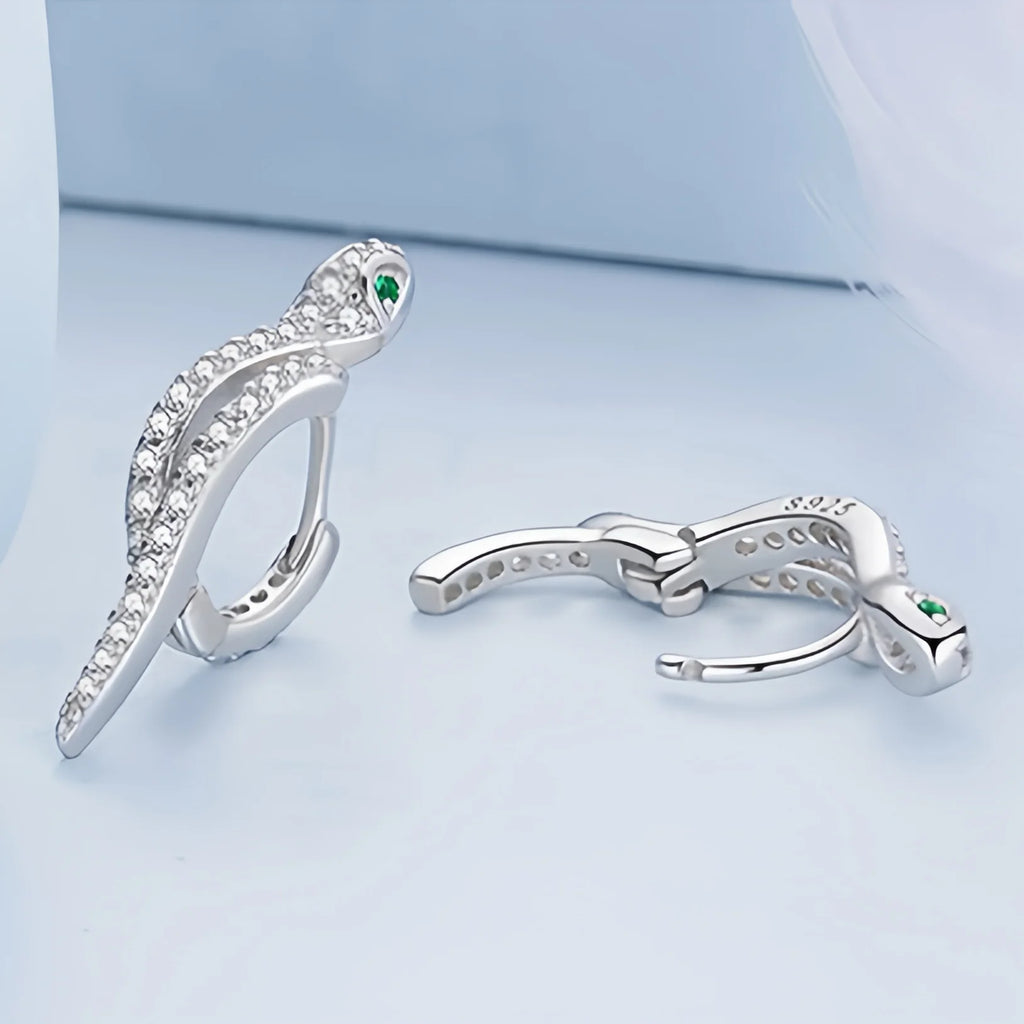 An elegant silver ring designed to resemble a serpent, adorned with numerous small crystals along its body. The snake's head is detailed with a pair of green crystal eyes, and the ring is stamped with 'S925' to indicate sterling silver purity.