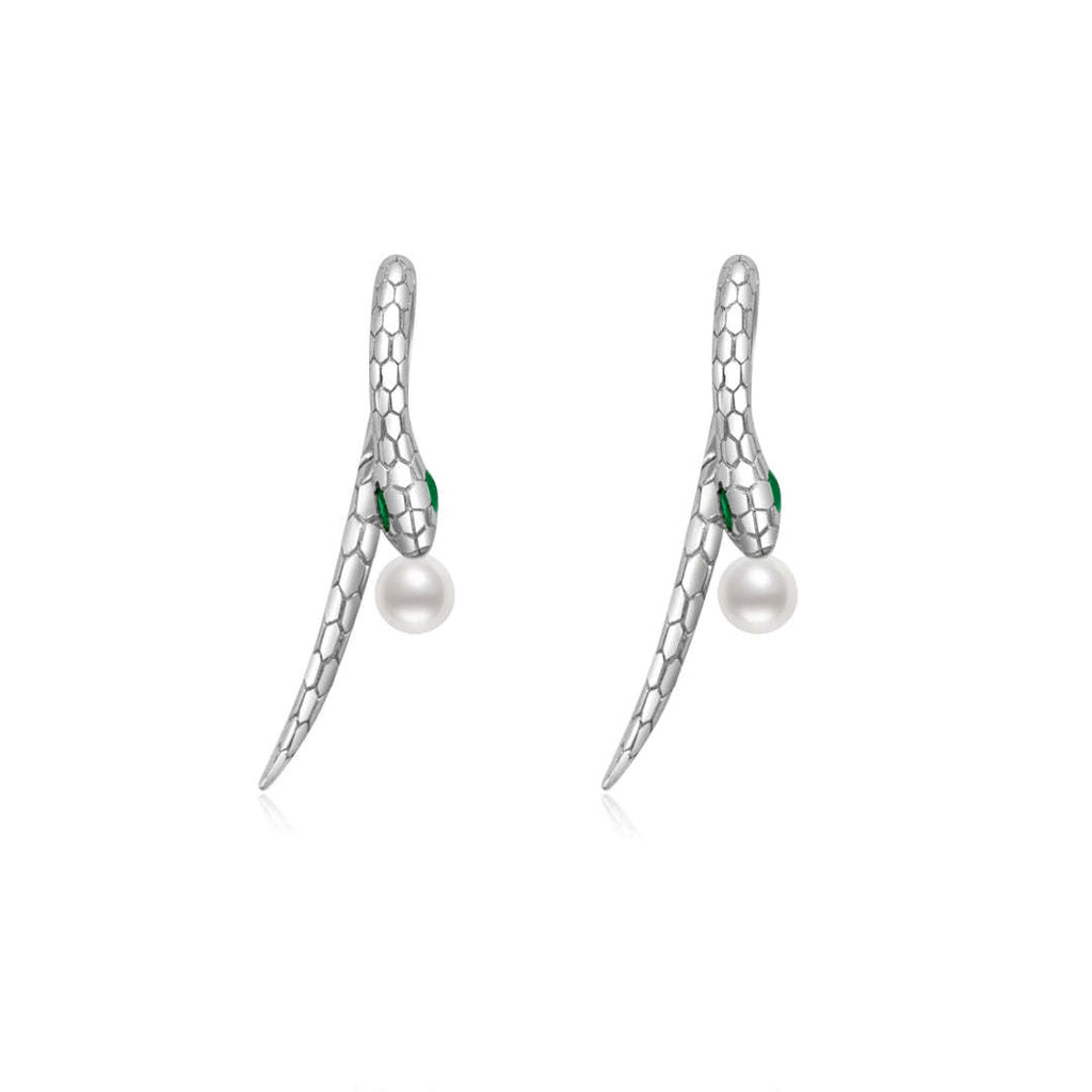 A pair of silver snake earrings, each featuring a detailed scale texture. The snakes have small green crystal eyes, adding a vibrant touch to the design. A classic white pearl dangles gracefully from the tail end of each snake, providing an elegant contrast to the silver metal.