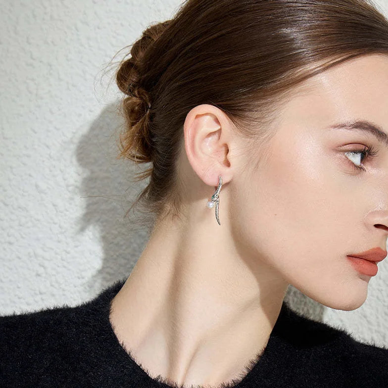 A profile view of a woman with a neatly styled bun, wearing a black top. She is adorned with a silver snake earring that curves along the contour of her ear, with small gemstone details and a pearl at the lower end, which provides an elegant touch to her minimalist appearance.