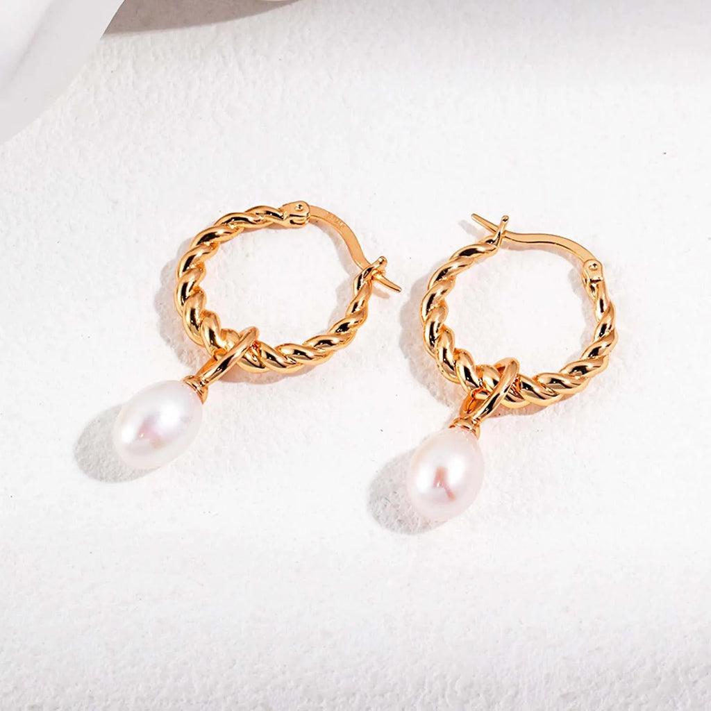 The image showcases a pair of silver hoop earrings with a twisted rope design, providing a sense of texture and depth to the metalwork. Each earring is adorned with a single round pearl pendant, which dangles elegantly below the hoop. The pearls have a soft, lustrous sheen that contrasts beautifully with the polished silver. The earrings are displayed on a white background with subtle shadows, highlighting the shine of the silver and the smoothness of the pearls.